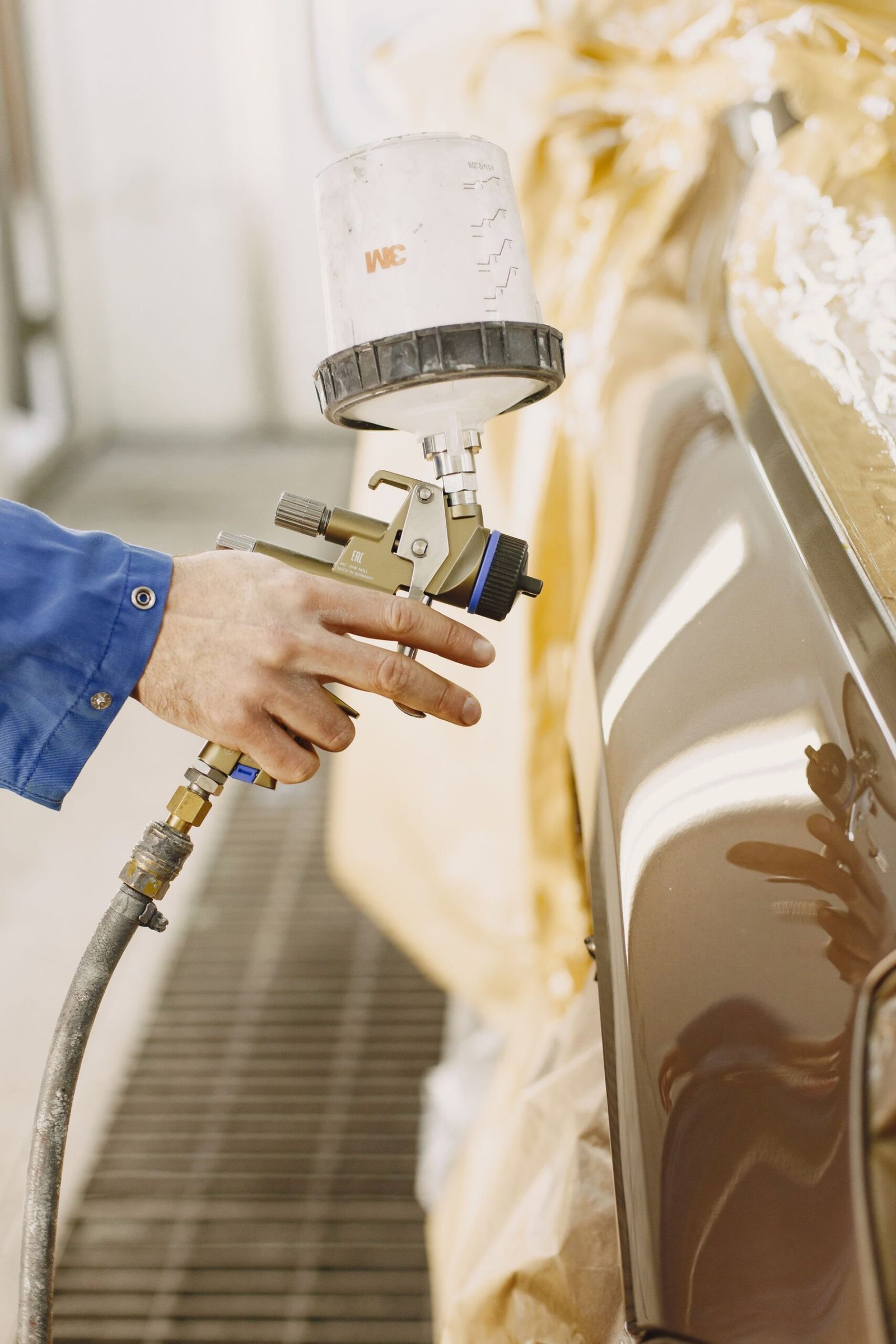 Technician spray painting a vehicle panel in an auto body shop